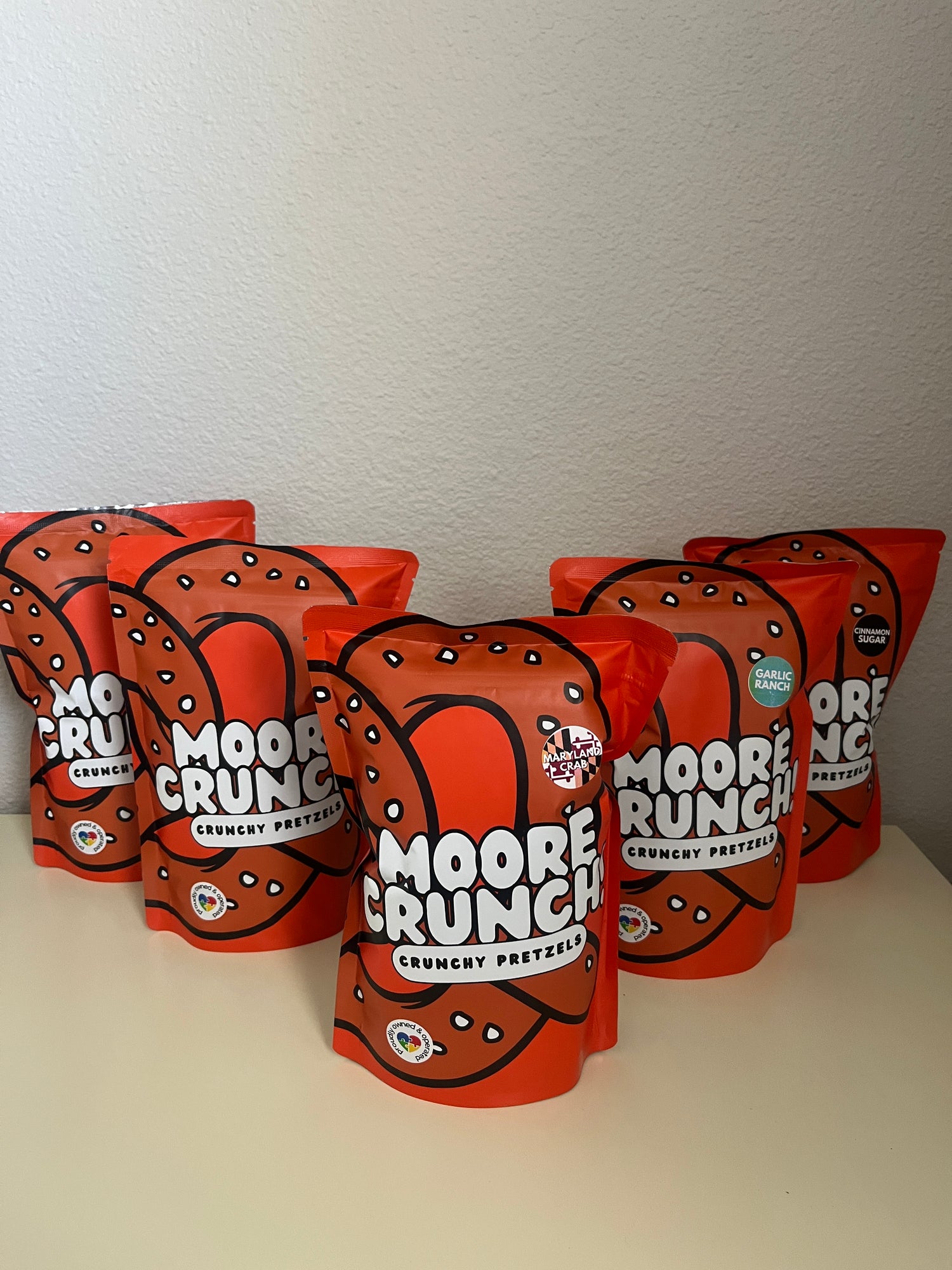 Multiple bags of Moore Crunch pretzels stacked on a white surface